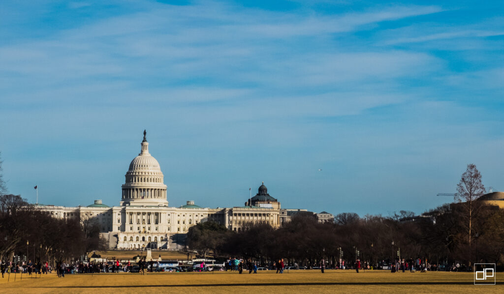 Capitol Building in Washington D.C. with a clear blue sky and people strolling on the foreground lawn