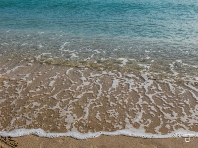 Gentle waves wash onto a sandy beach with white foam along the shoreline