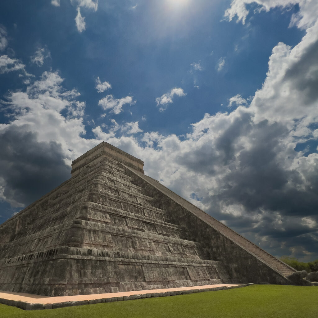 Stone stepped pyramid with broad terraces and a grassy foreground under a cloudy blue sky.