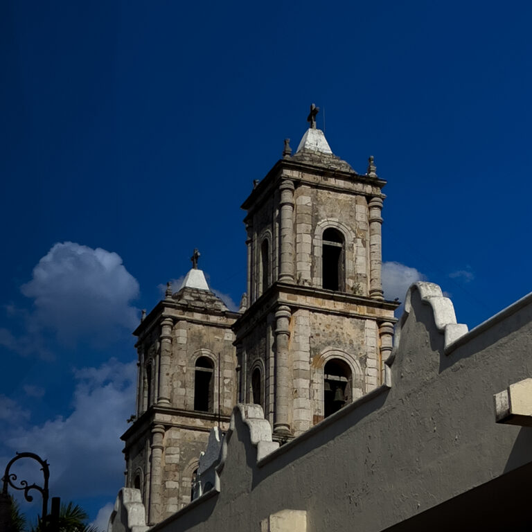 Stone church tower with rounded arched openings and decorative pinnacles under a clear blue sky far above ground level.