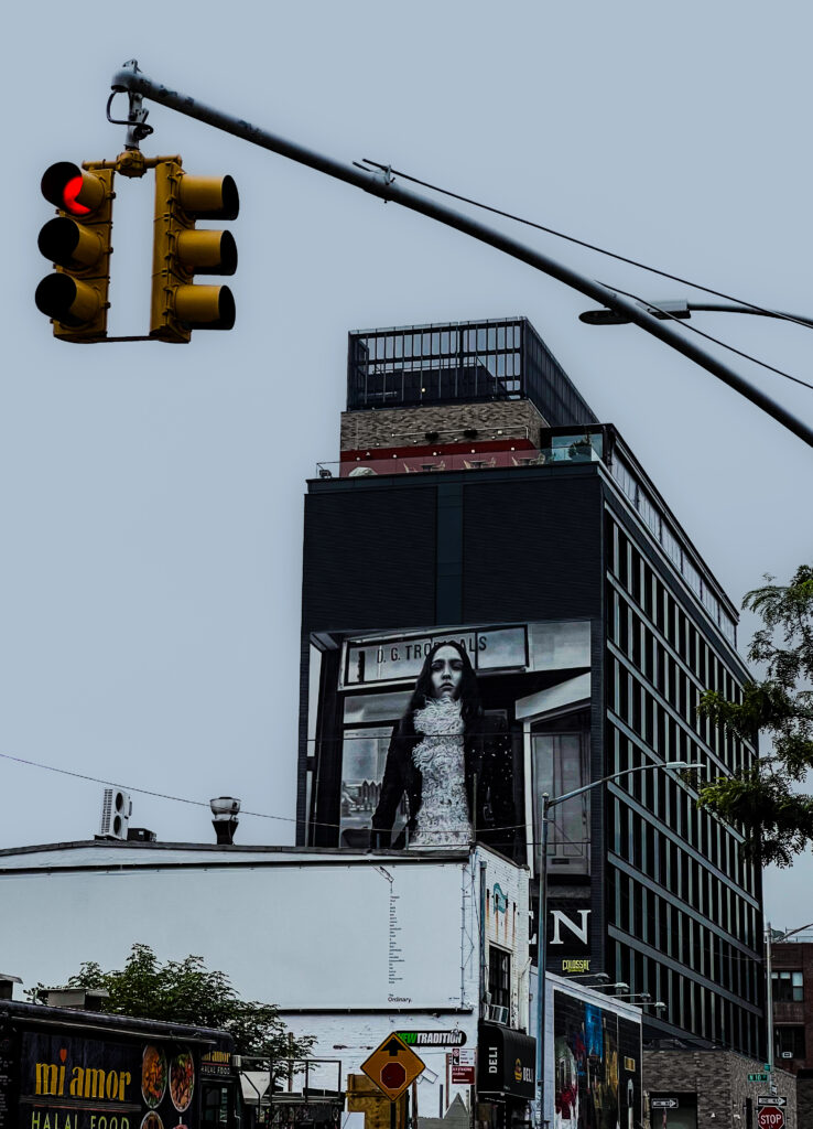 Yellow traffic light with a red signal at an urban intersection, against a tall modern building with a large fashion billboard.