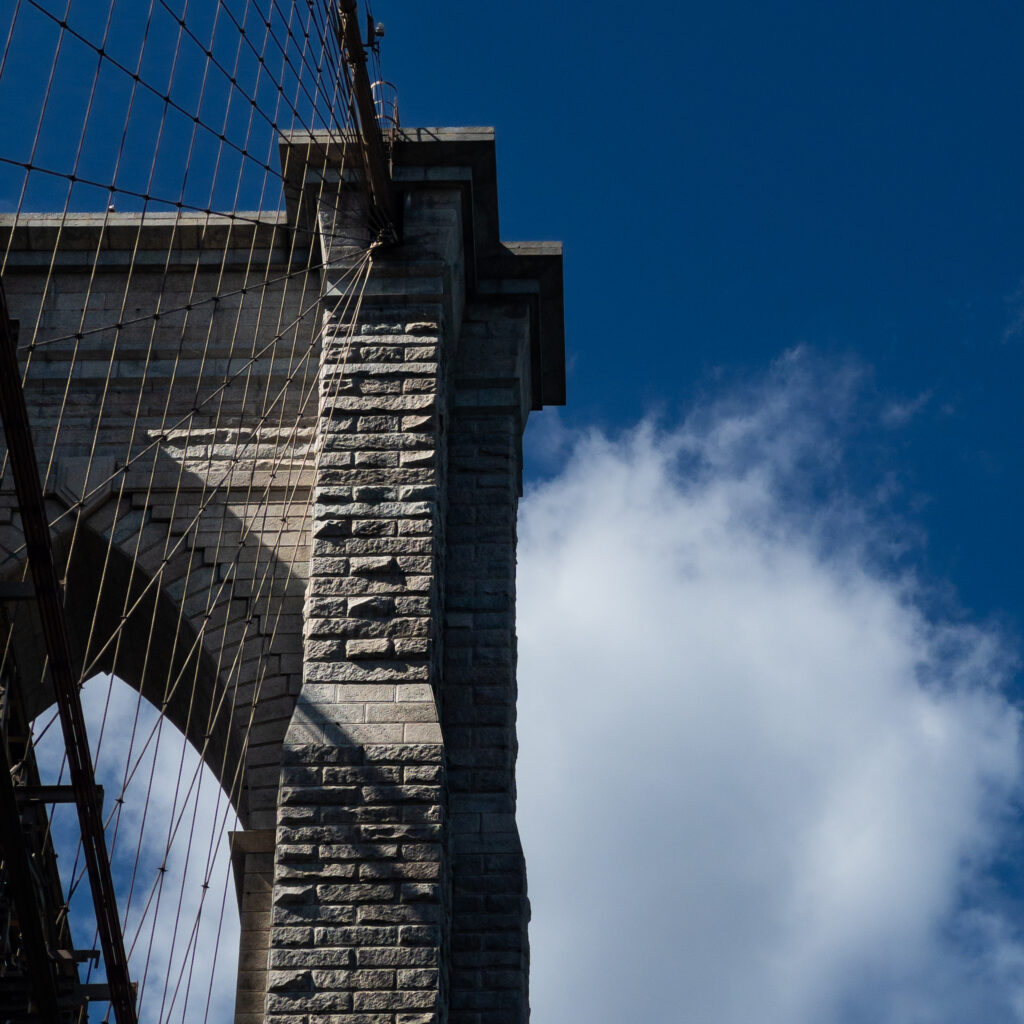 Close-up of a stone bridge tower with numerous steel suspension cables against a clear blue sky.