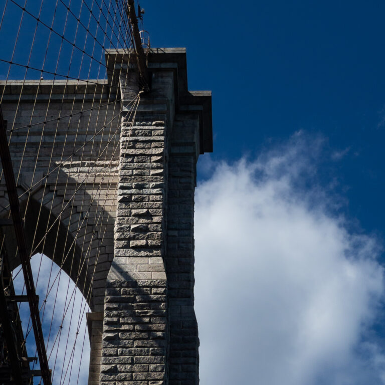 Close-up of a stone bridge tower with numerous steel suspension cables against a clear blue sky.