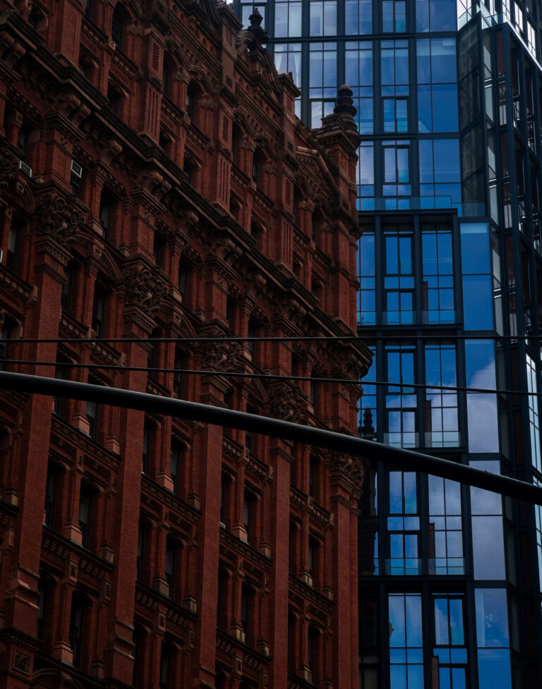 Two contrasting buildings: a red brick historic façade with ornate detailing beside a blue-glass modern skyscraper.