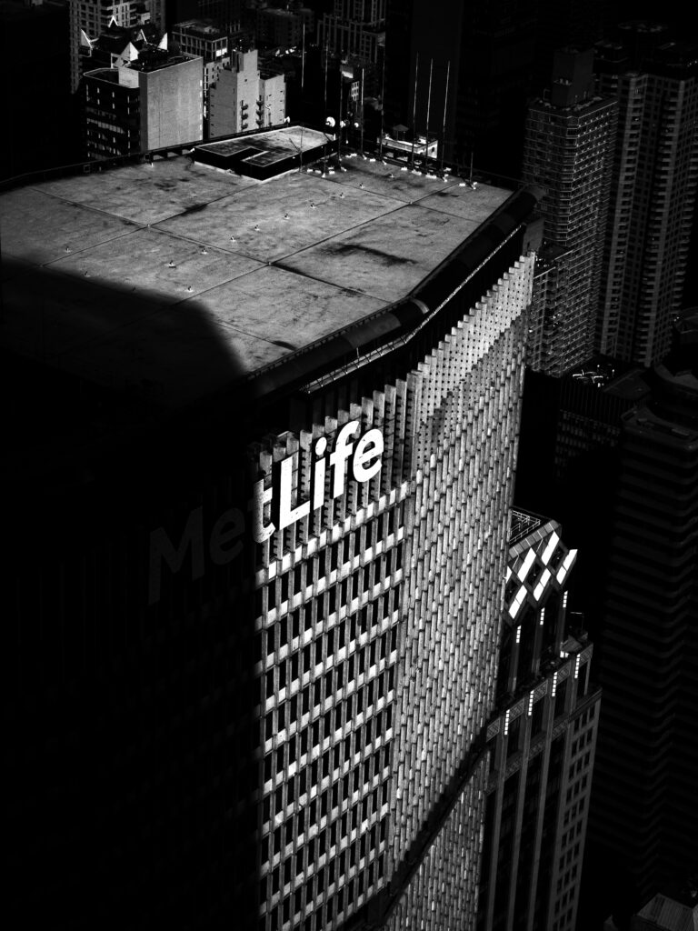 Aerial night view of a tall city block; the side of a building shows a large MetLife sign, with surrounding skyscrapers in the background.