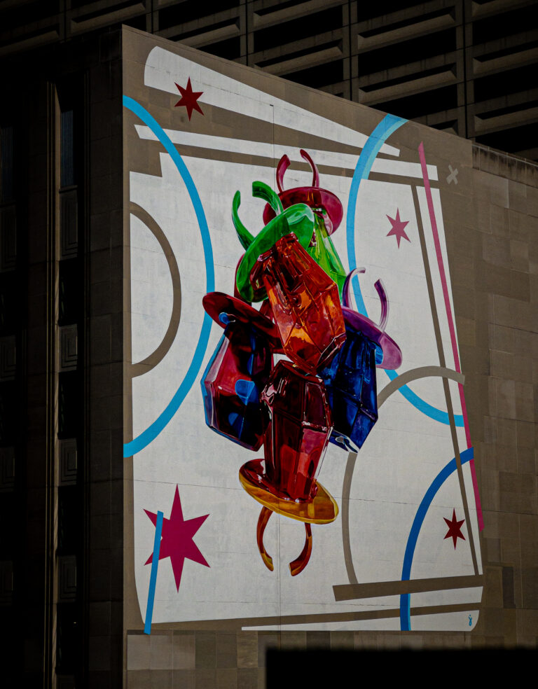 Colorful glass sculpture mounted on a wall mural with blue curves and pink stars in an urban setting.