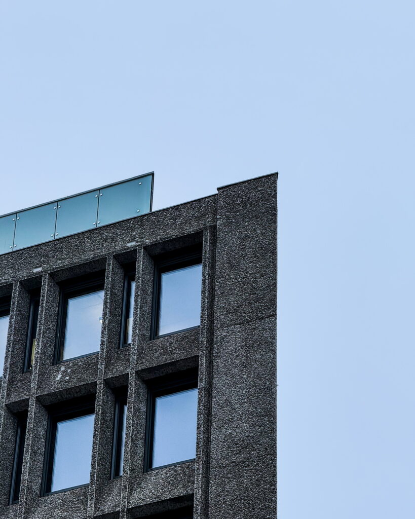 Corner of a textured concrete building with large rectangular windows against a clear blue sky.