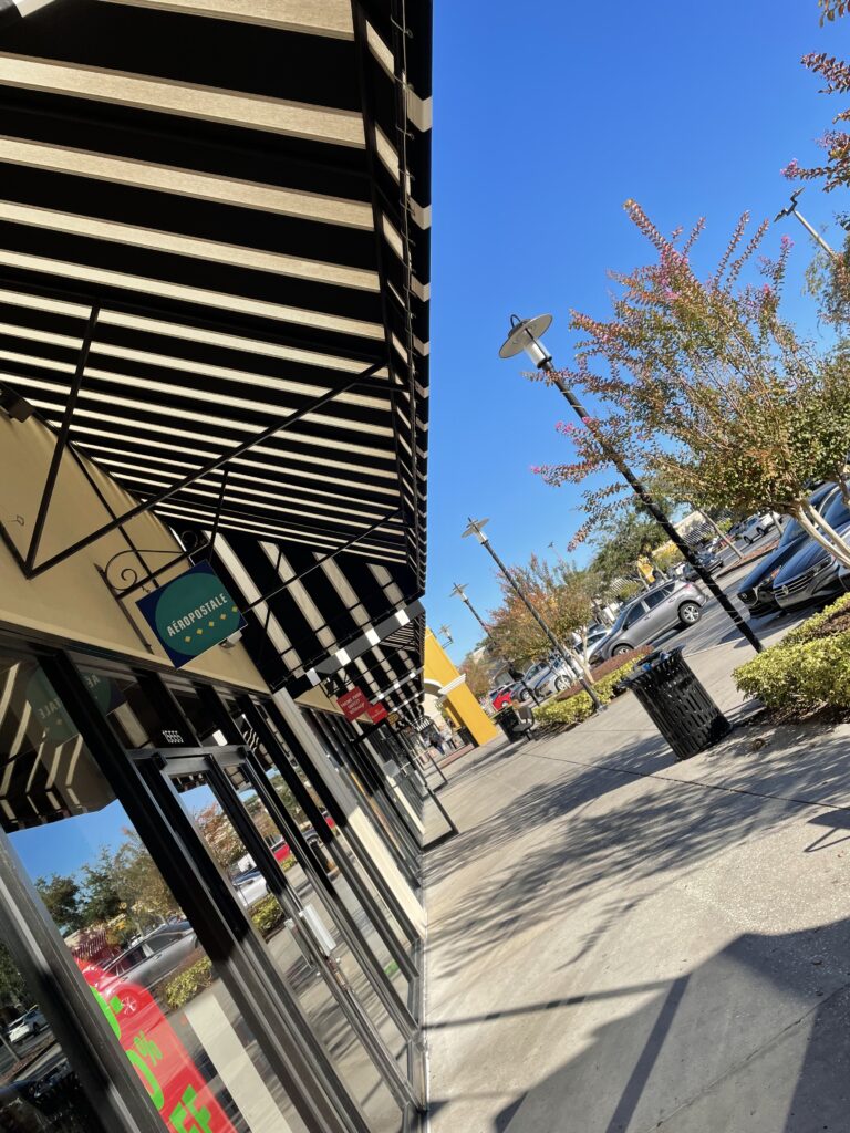 Storefront with black-and-white striped awning, glass doors, and a blue sky; trees with pink blossoms line the sidewalk.